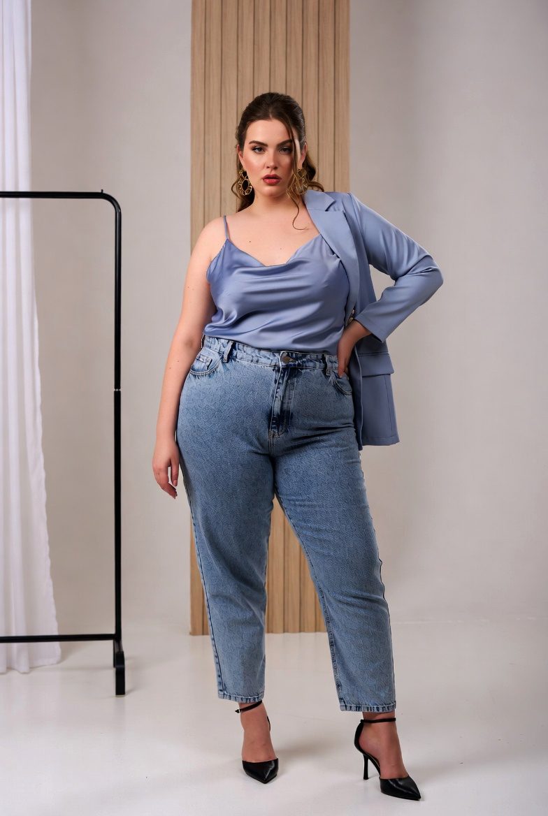 Plus-size model in mom jeans, silk camisole, and tailored blazer posing confidently against a minimalist background.