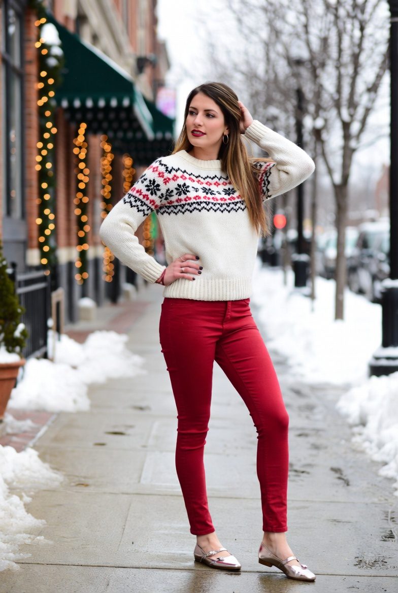 Slim white woman wearing a white knit Christmas sweater and red skinny pants with metallic flats, classic festive winter outfit.